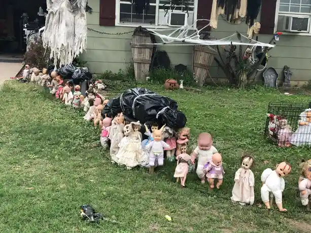 A yard decorated for Halloween is filled with dozens of creepy, old-fashioned baby dolls arranged in rows on the grass, some…
