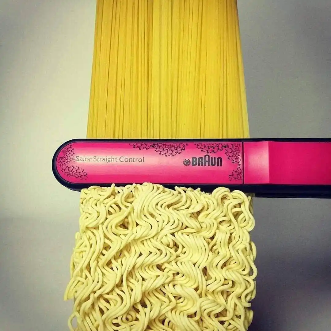 A pink Braun SalonStraight Control hair straightener is positioned horizontally, with a bundle of straight, uncooked…