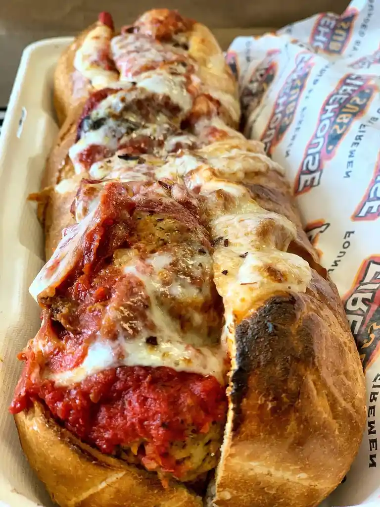A close-up photo of a long, sliced meatball sub from Firehouse Subs, showing layers of meatballs, tomato sauce, and melted…