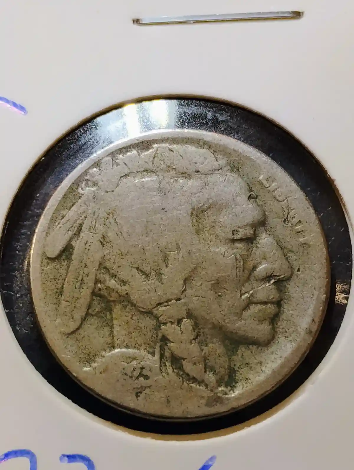 A close-up of a heavily worn and tarnished silver-colored coin, likely a Buffalo nickel, showing a profile of a Native…