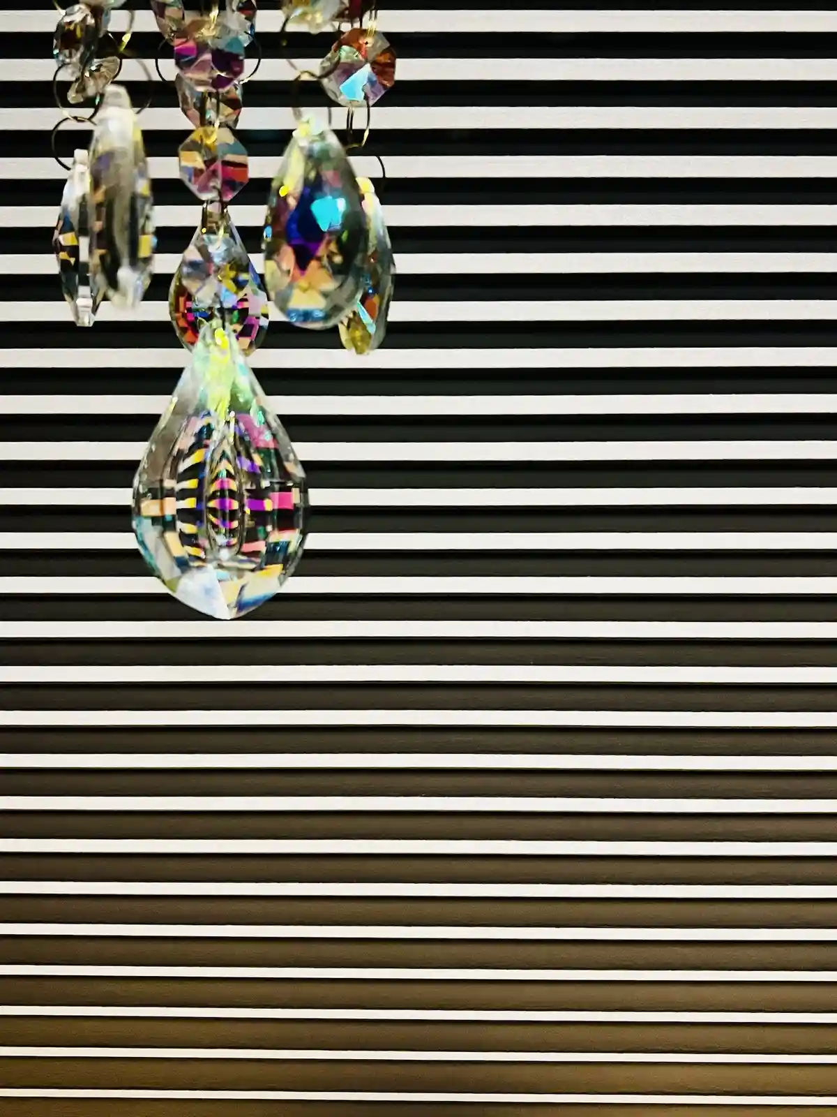 A close-up photo shows a colorful, faceted crystal ornament hanging against a background of black and white horizontal…