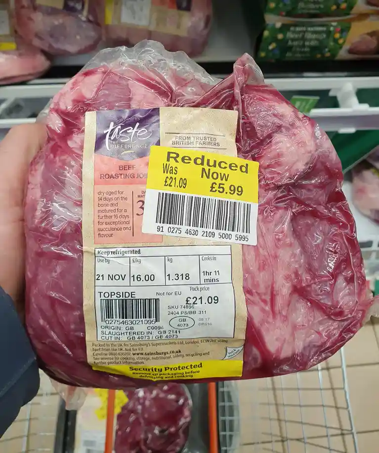 A hand holds a Sainsbury's beef roasting joint in plastic packaging, showing a yellow price tag that says 'Reduced Was…