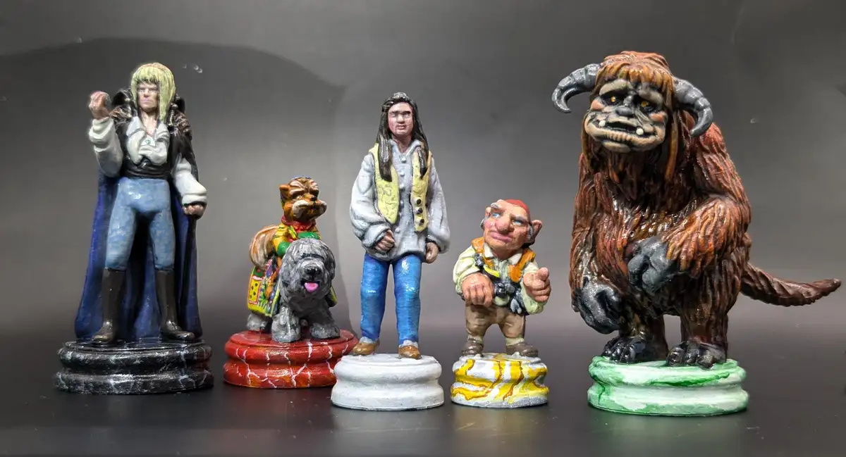 Five hand-painted fantasy miniatures stand in a row on different colored bases against a dark background. From left to…