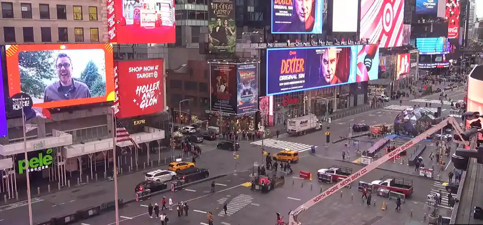 A high-angle photo of Times Square, New York, filled with bright billboards, pedestrians, and traffic. One large billboard…