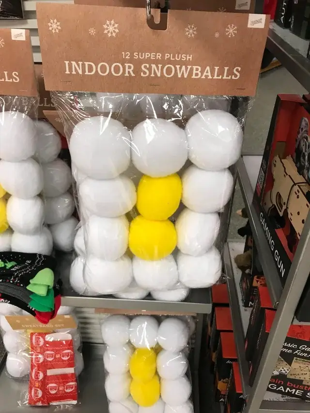 A retail shelf displays packages of white plush snowballs, with one package featuring two yellow snowballs in the center…