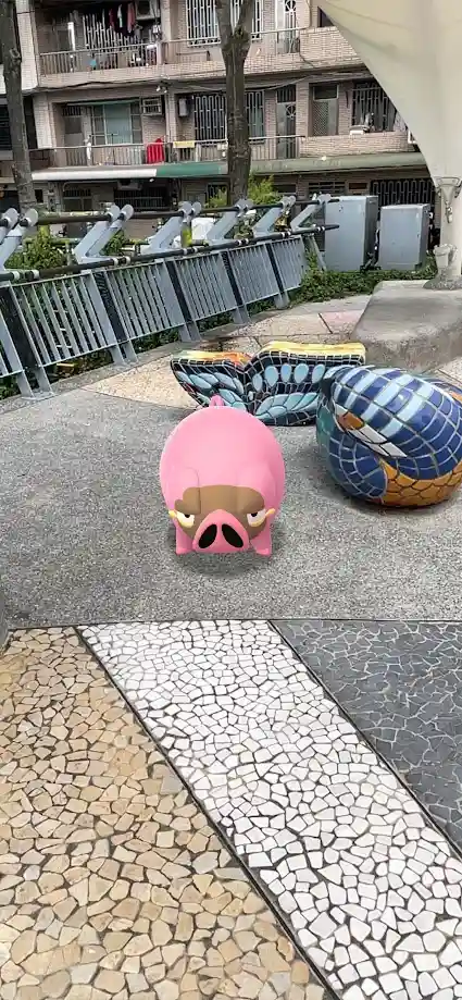 A pink cartoon pig with a grumpy expression is superimposed on a paved outdoor area with mosaic tiles and colorful benches…