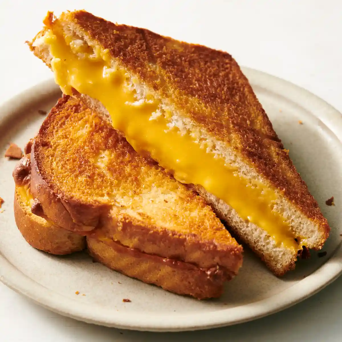 A close-up of a perfectly grilled cheese sandwich, cut in half and stacked, with molten yellow cheese oozing out from…