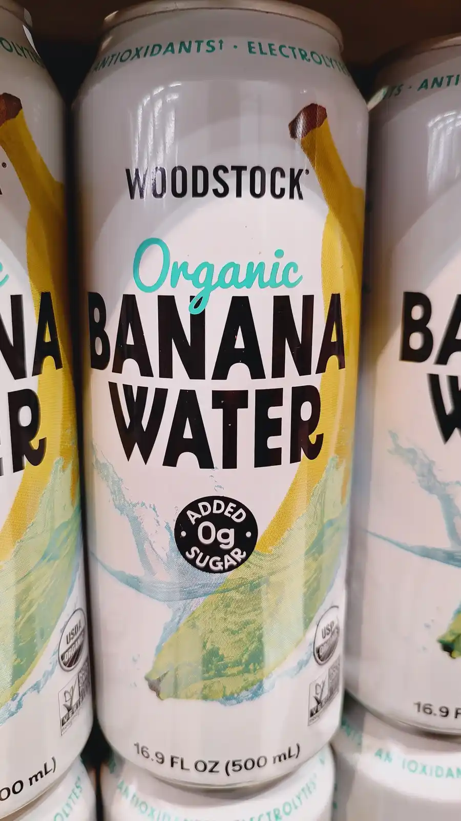A close-up photo shows a can of Woodstock Organic Banana Water, with text indicating 'Added 0g Sugar'. The can features a…
