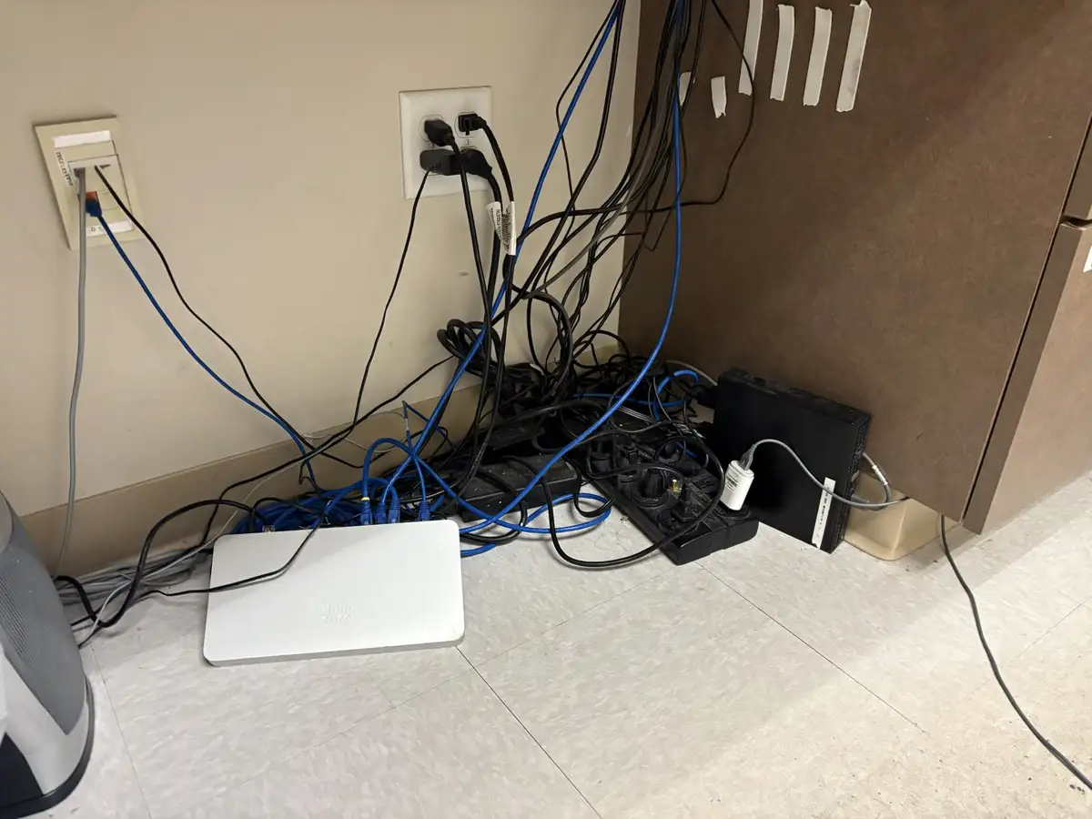 A messy tangle of blue ethernet cables and black power cords sprawls across a tiled floor near wall outlets, connecting to a…