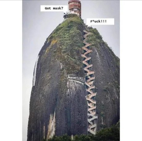 A steep, narrow staircase spirals up a sheer, moss-covered rock face toward a tower at the summit. Two white text boxes are…