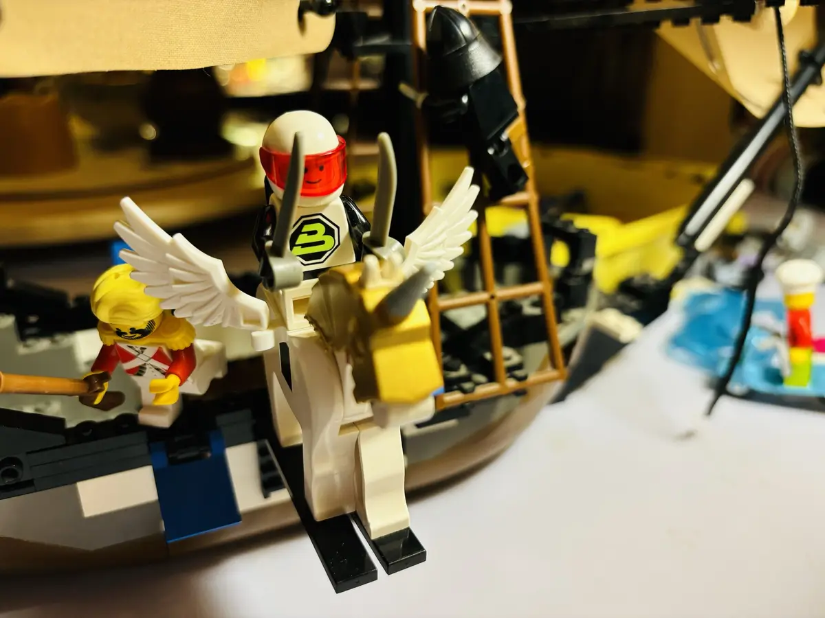 A close-up photo shows a LEGO minifigure with white wings and a red visor, standing on black skis while holding two gray…