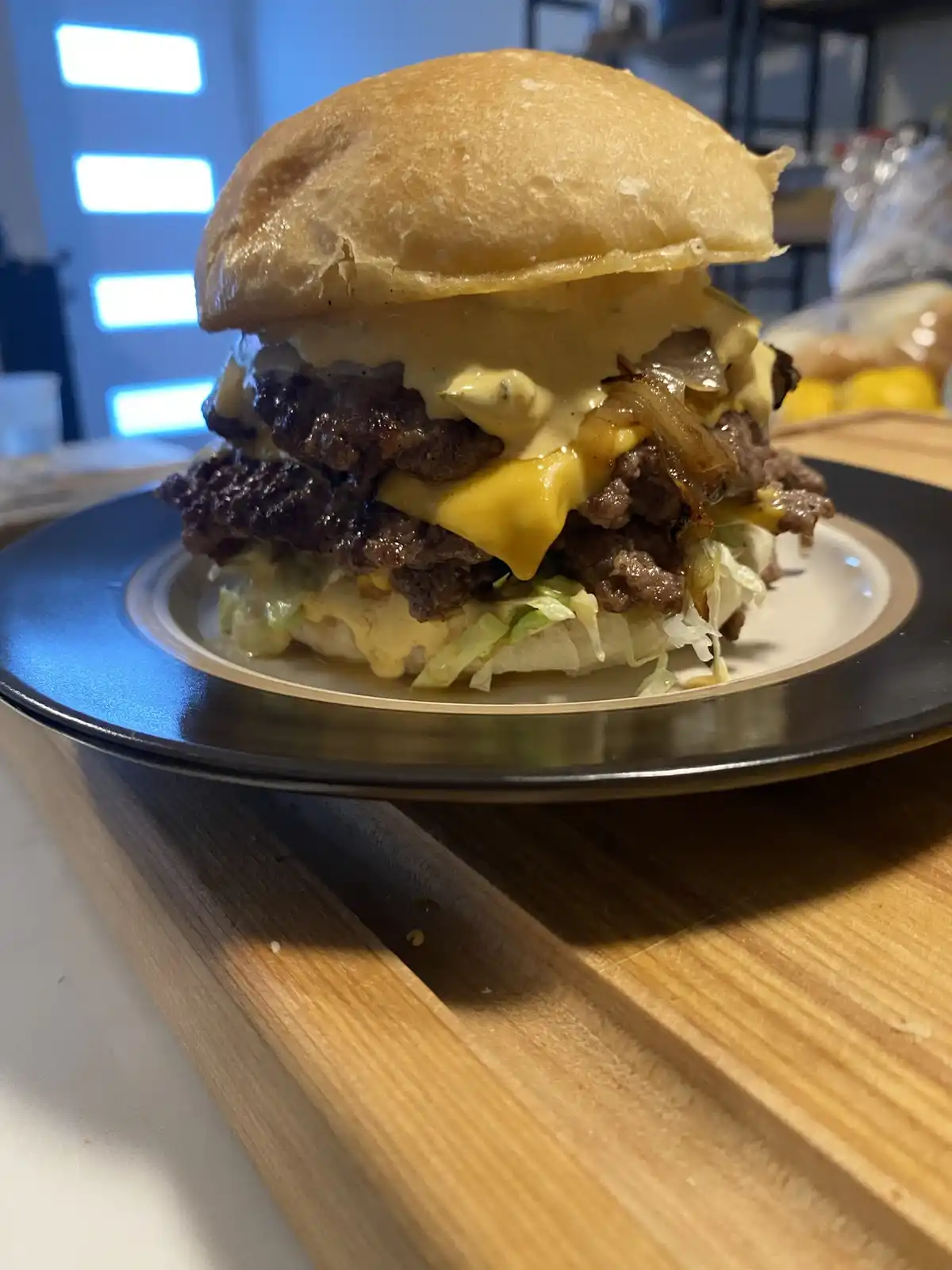 A close-up photo of a tall, messy double burger with melted cheese, caramelized onions, and sauce, sitting on a plate on a…