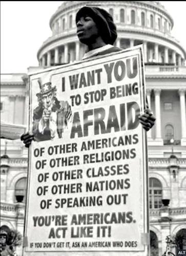 A black-and-white photo shows a Black person holding a large protest sign in front of the U.S. Capitol building. The sign…