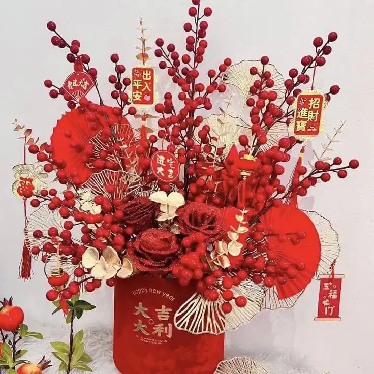 A vibrant red floral arrangement in a red cylindrical vase, decorated with red berries, glittery red roses, white paper…