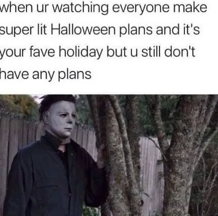 A still image of Michael Myers from Halloween, standing outdoors beside a tree with a wooden fence in the background…