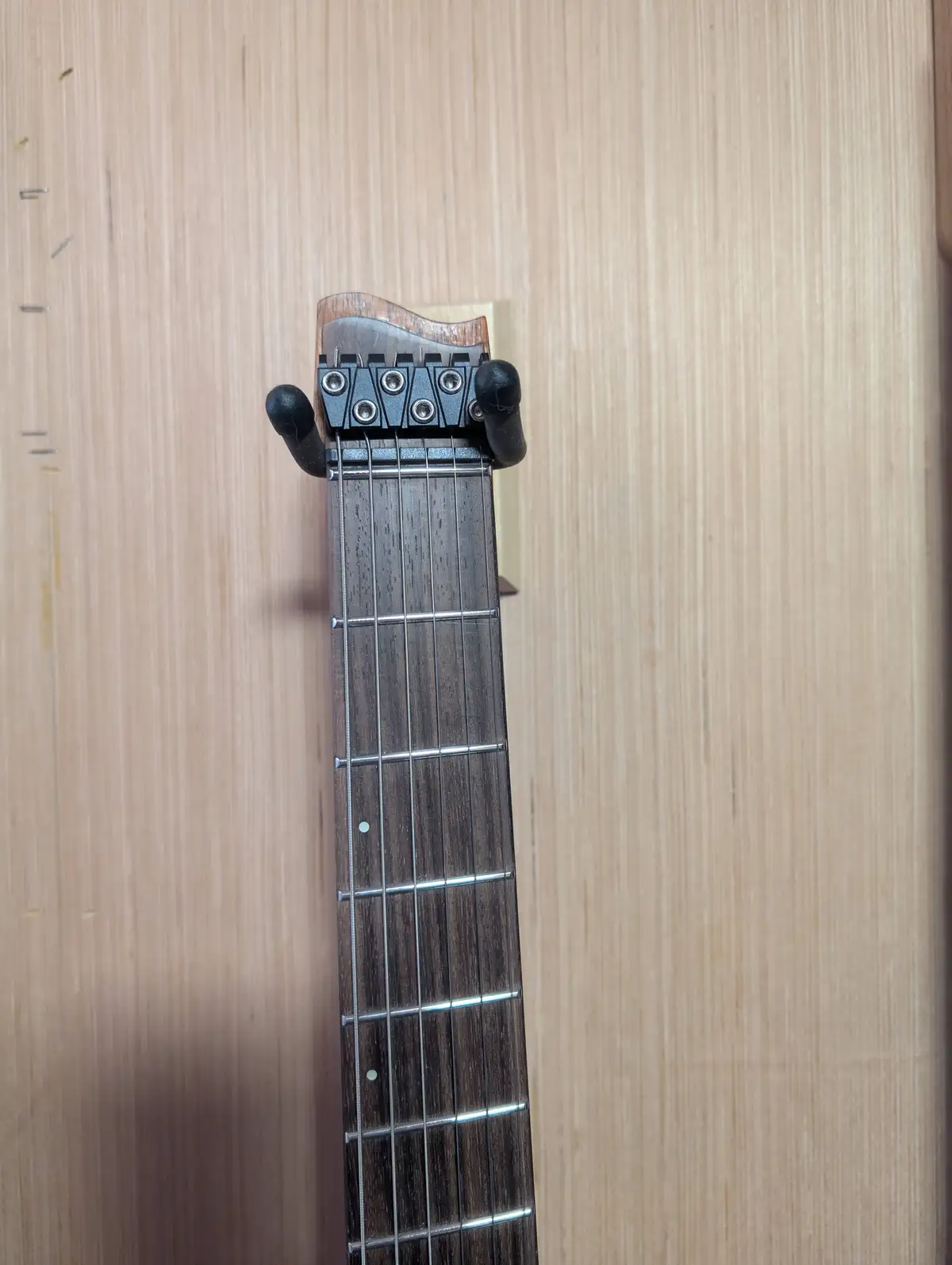 A close-up photo of a guitar neck with a black metal tuning peg headstock against a light wood background. The overlaid text…