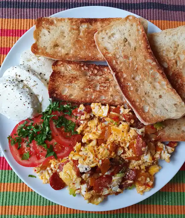 A plate of breakfast food including scrambled eggs with tomatoes and sausage, sliced tomatoes with parsley, mozzarella…