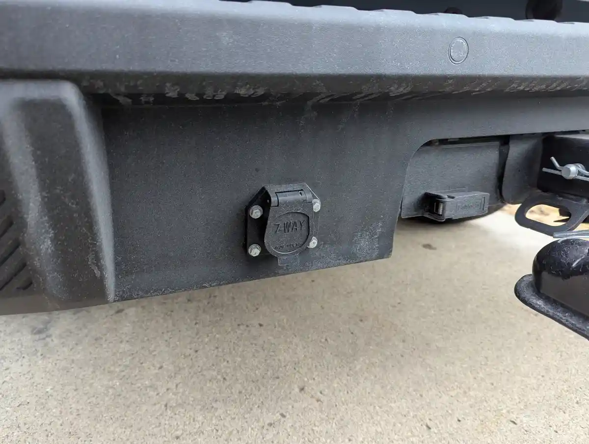 A close-up photo shows the rear of a vehicle, focusing on a black 7-way trailer hitch connector labeled '7-WAY 12 VOLTS'…