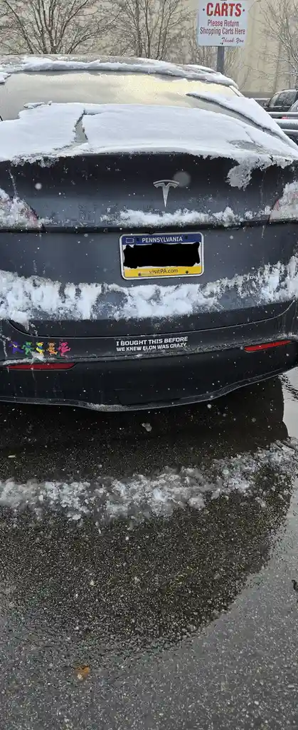 The rear of a black Tesla Model X covered in snow and ice, parked in a snowy lot. The Pennsylvania license plate is…