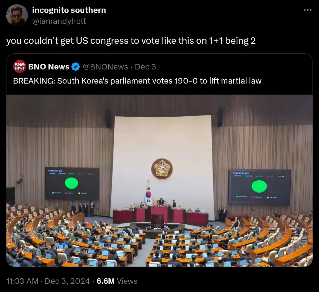 An image of South Korea's parliamentary chamber with members seated in a semi-circle, two large screens showing a green…