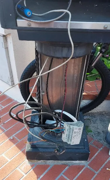 A close-up photo shows the base of an outdoor electrical device, possibly a streetlight or utility box, with tangled wires…
