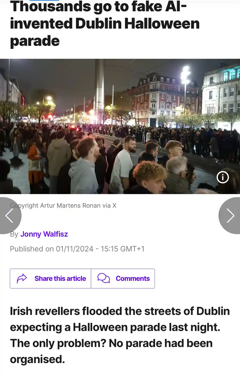A nighttime photo shows a large crowd of people gathered along a city street in Dublin, looking expectantly toward the road…