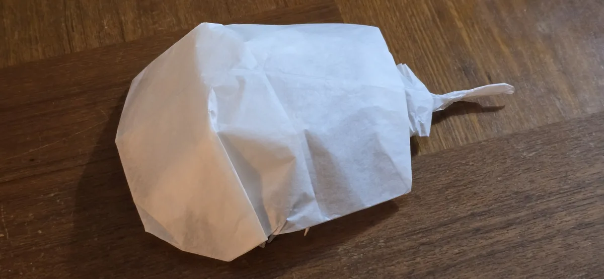 A crumpled white paper bag, resembling a ghost or a wrapped object, rests on a wooden floor. The overlaid text reads 'i'm…