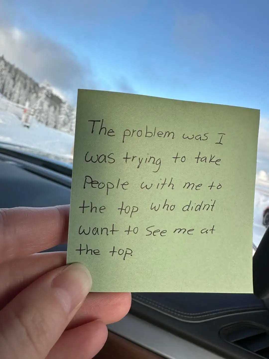 A hand holds a green sticky note inside a car, with handwritten text reading 'The problem was I was trying to take people…