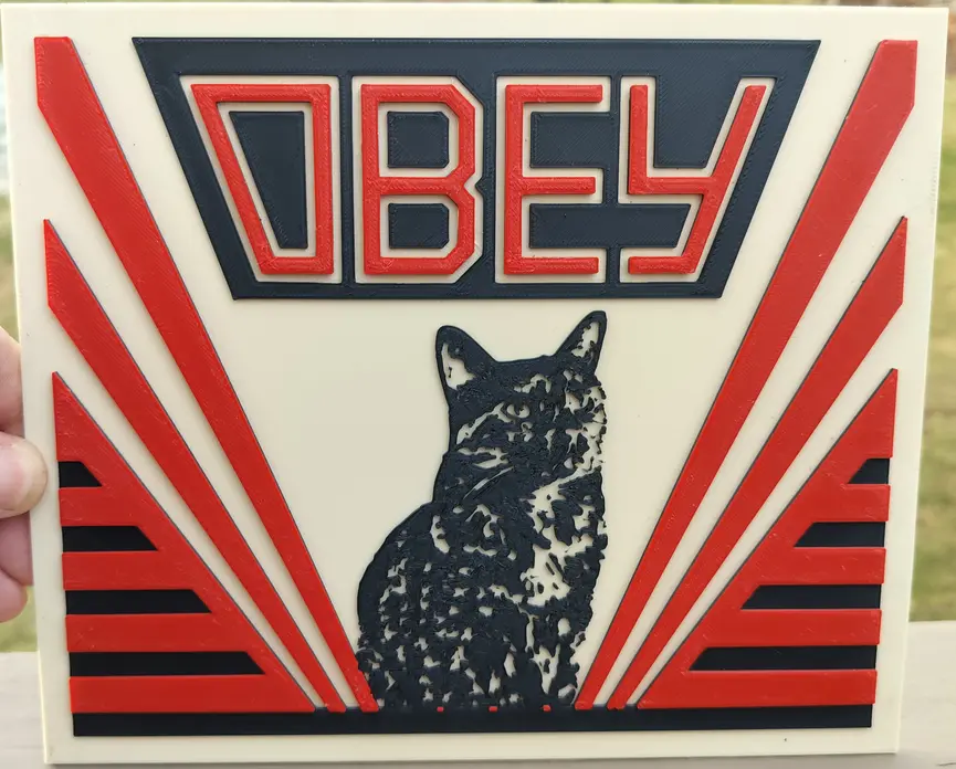A 3D-printed plaque features the word 'OBEY' in bold red and black lettering at the top, above a black-and-white silhouette…