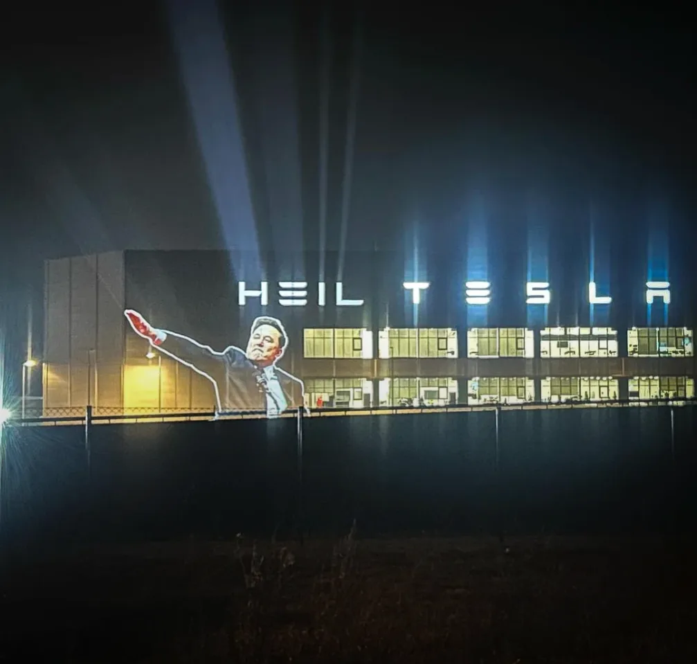 A nighttime photo of a large building with bright spotlights shining upwards. The building's facade displays the text 'HEIL…