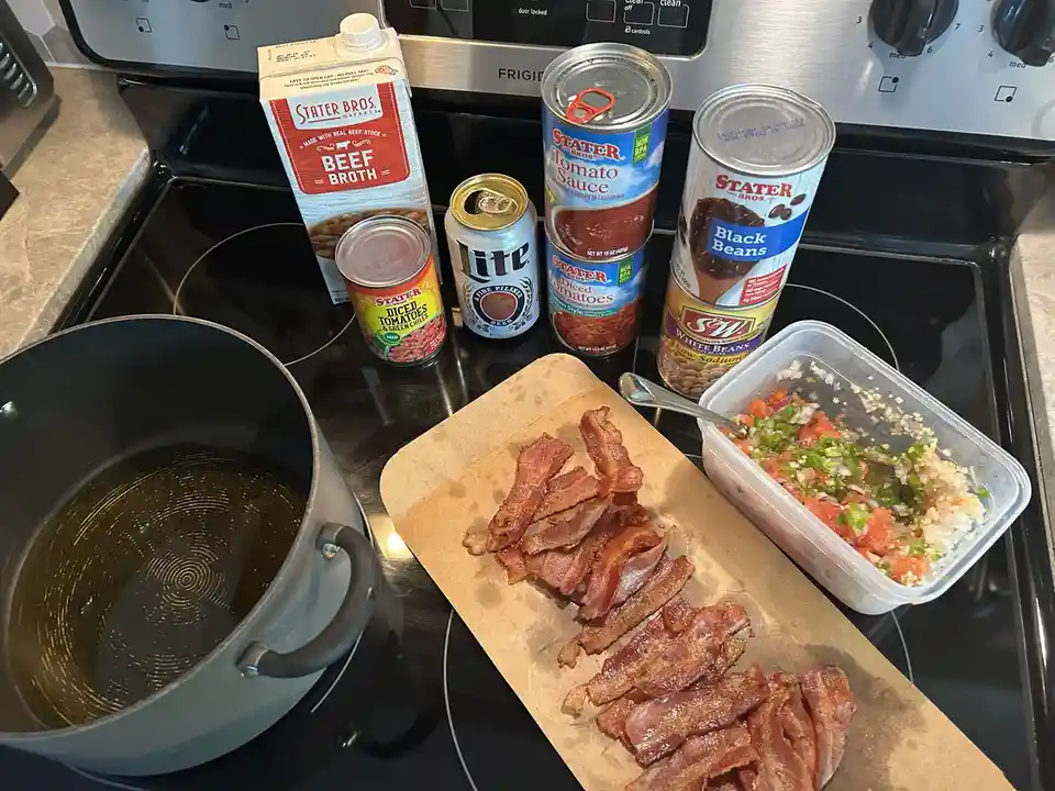 A kitchen stovetop displays a large pot, a pile of cooked bacon on parchment paper, a container of pico de gallo, and…