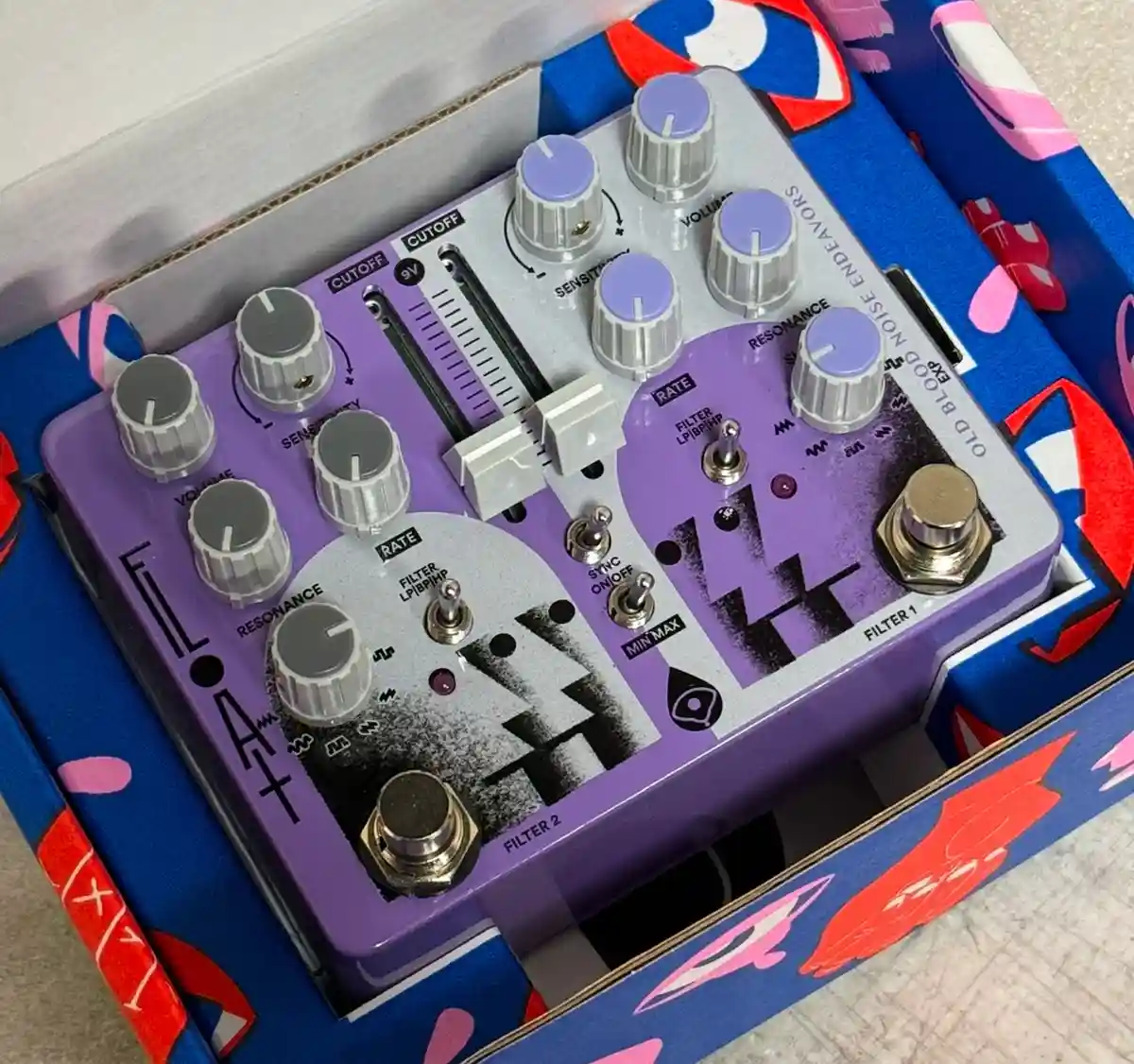A purple and silver guitar effects pedal labeled 'FLOAT' by 'OLD BLOOD NOISE ENDEAVORS' sits inside its colorful box…