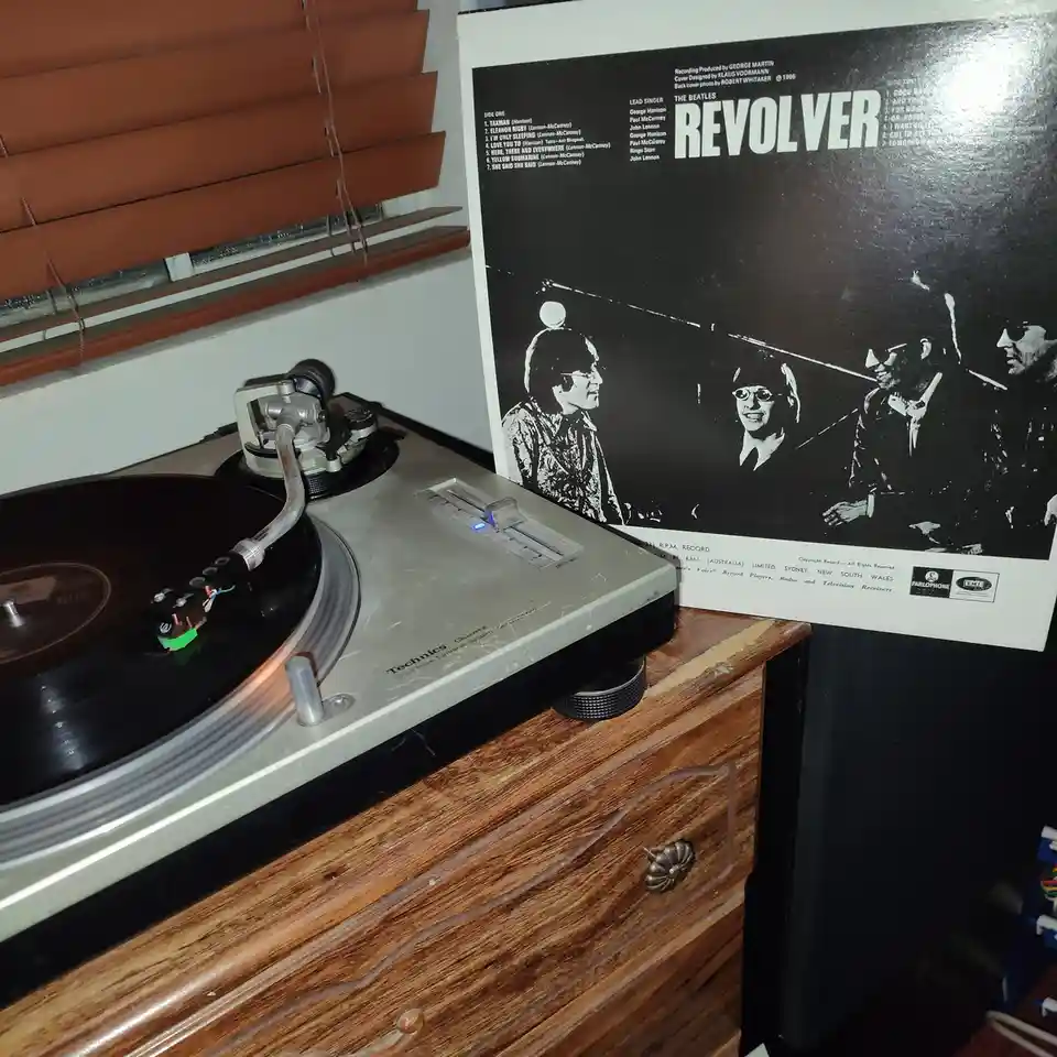 A Technics turntable sits on a wooden dresser with a vinyl record spinning, next to the back cover of The Beatles'…