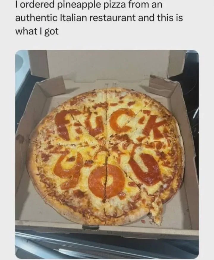 A pizza in a cardboard box has the word 'FUCK YOU' spelled out using pepperoni slices as letters on top of melted cheese and…