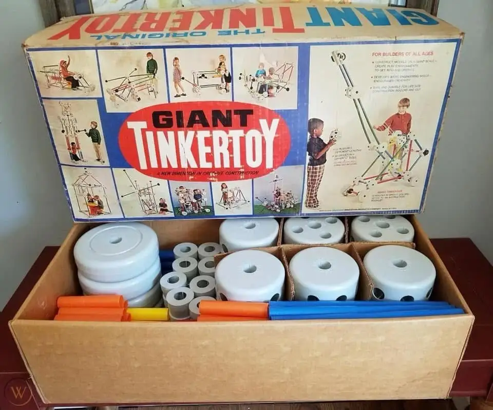 An open cardboard box labeled 'GIANT TINKERTOY' displays large, oversized construction toy pieces including white circular…