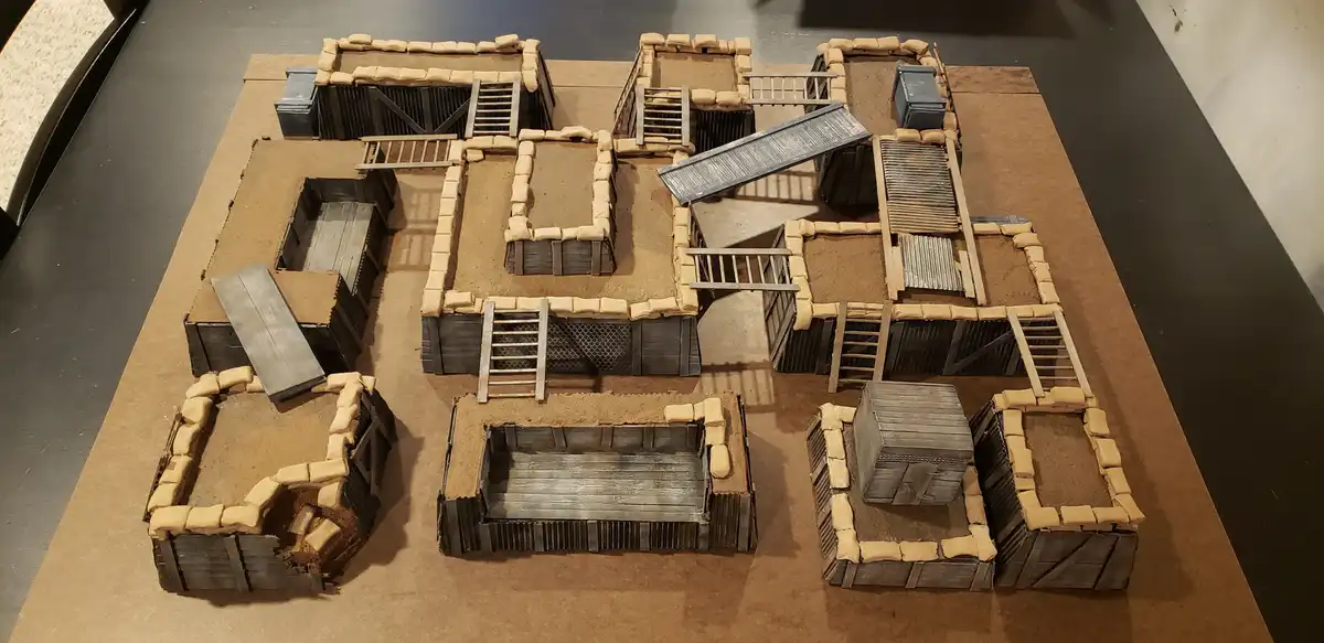 An overhead view of a detailed miniature model depicting a complex trench system made of sandbags, wooden planks, and…