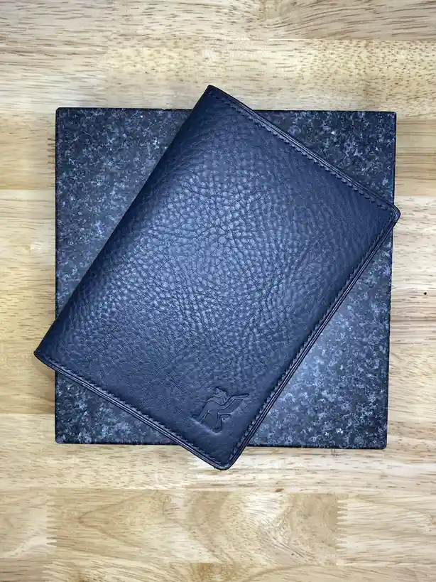 A dark blue textured leather wallet with a lion logo embossed on the bottom corner rests diagonally atop a dark gray…