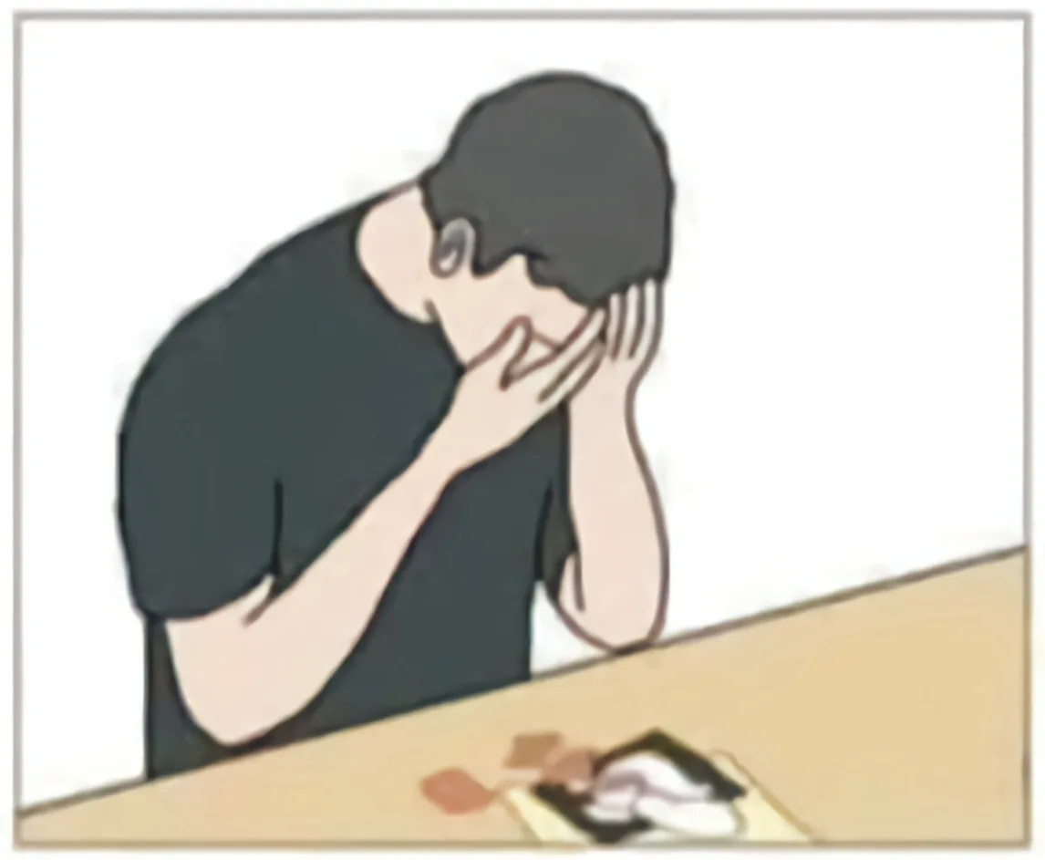 A cartoon person in a black t-shirt is slumped over a table, covering their face with both hands in a gesture of despair or…