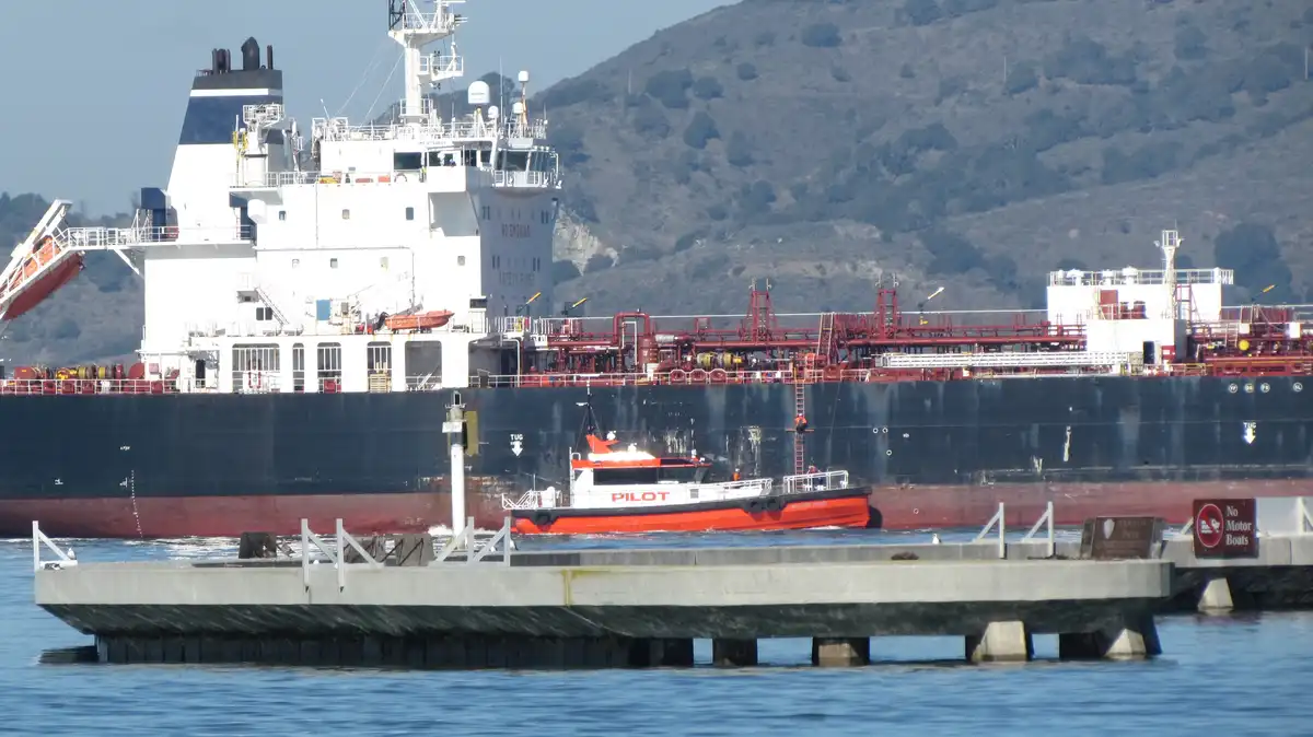 A large cargo ship named 'WEST VIRGINIA' is docked near a pier, with a small red and white pilot boat labeled 'PILOT'…
