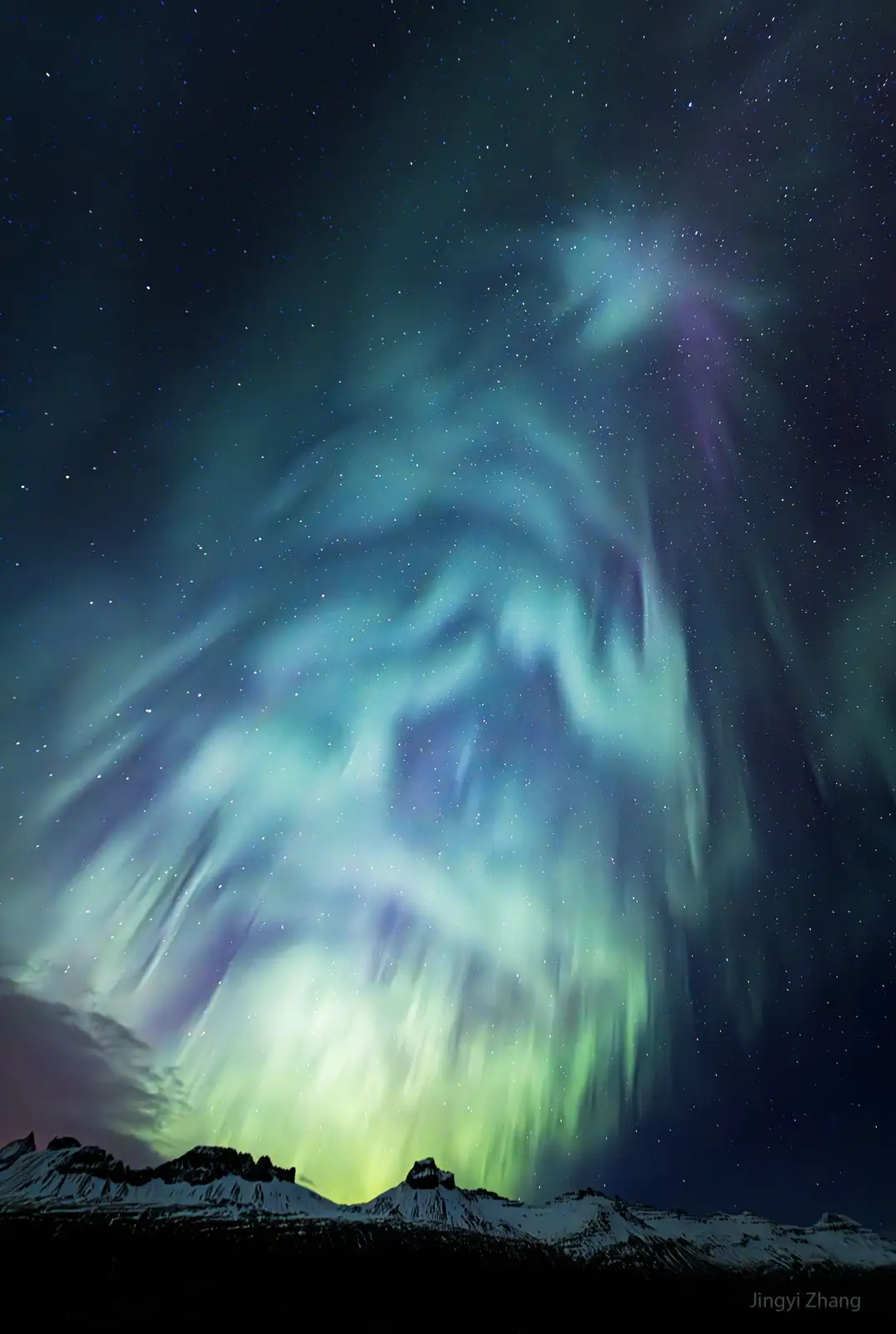 A stunning photograph of the aurora borealis dancing across a starry night sky above snow-capped mountains, with the…