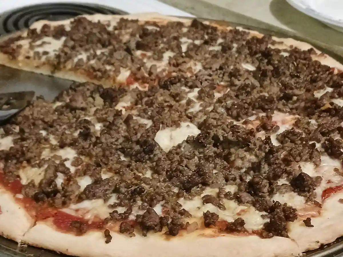 A close-up photo of a homemade pizza on a metal tray, covered in melted cheese and a generous layer of cooked ground beef…