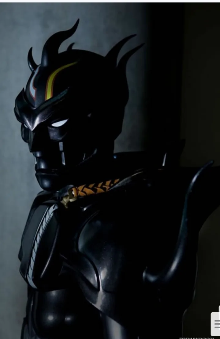 A dark, menacing figure in a black armored suit with horn-like protrusions on the helmet and glowing white eyes, standing in…