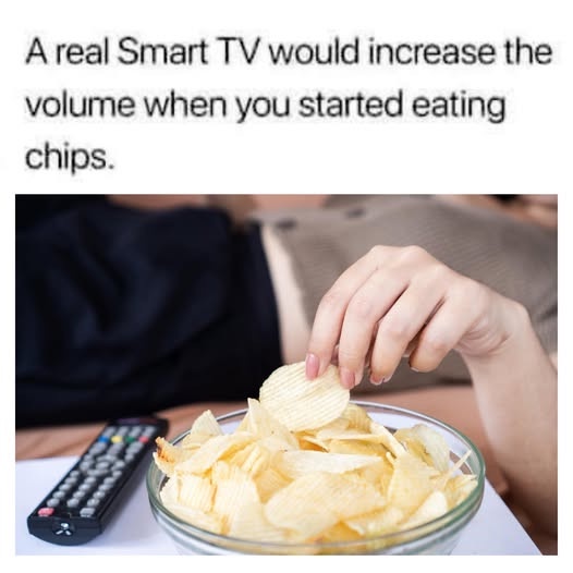 A person's hand reaches into a glass bowl of ridged potato chips while a TV remote lies nearby on a surface. The overlaid…