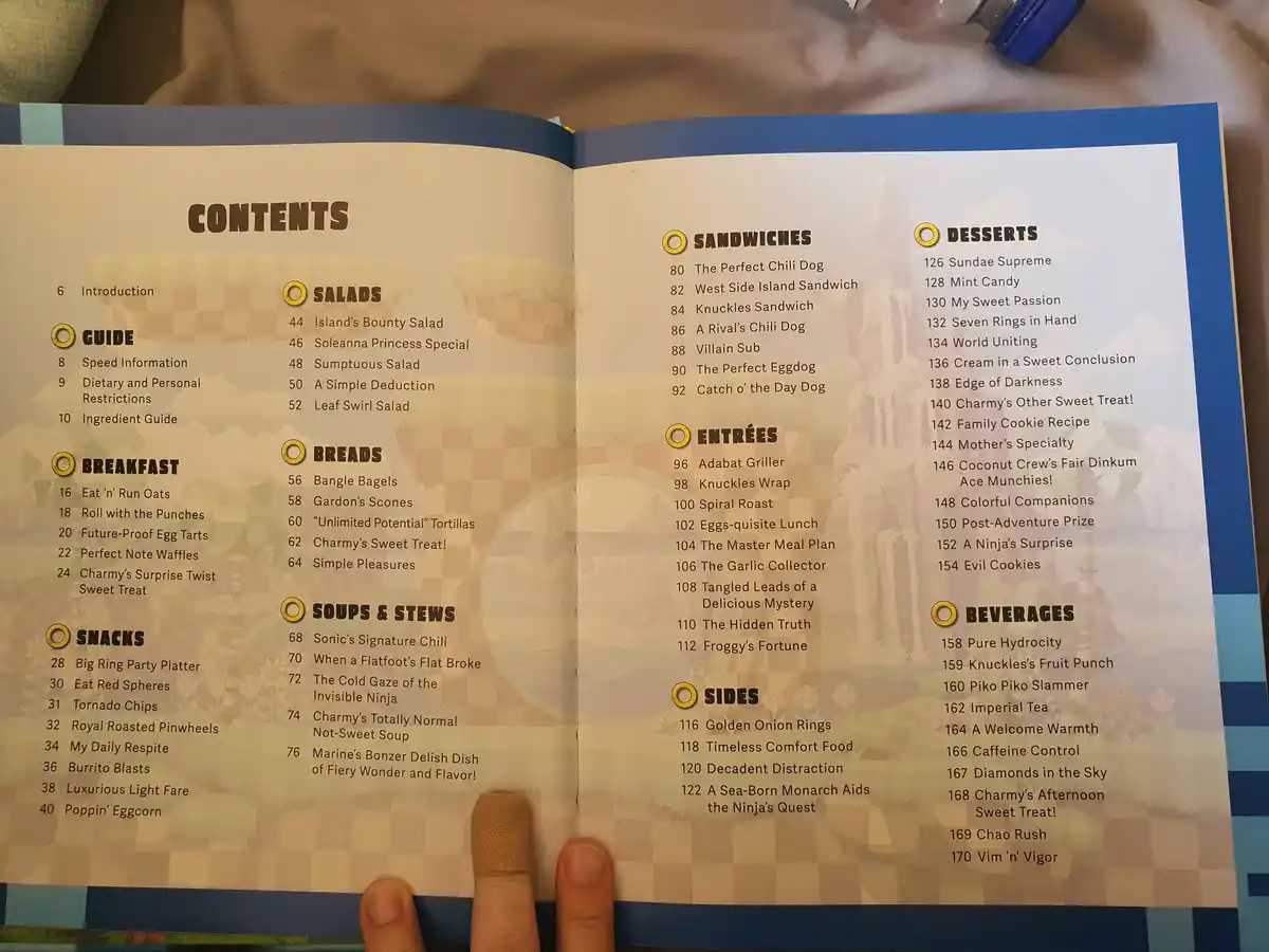 An open cookbook displays a 'CONTENTS' page listing food categories like Salads, Sandwiches, Entrées, and Desserts, with…