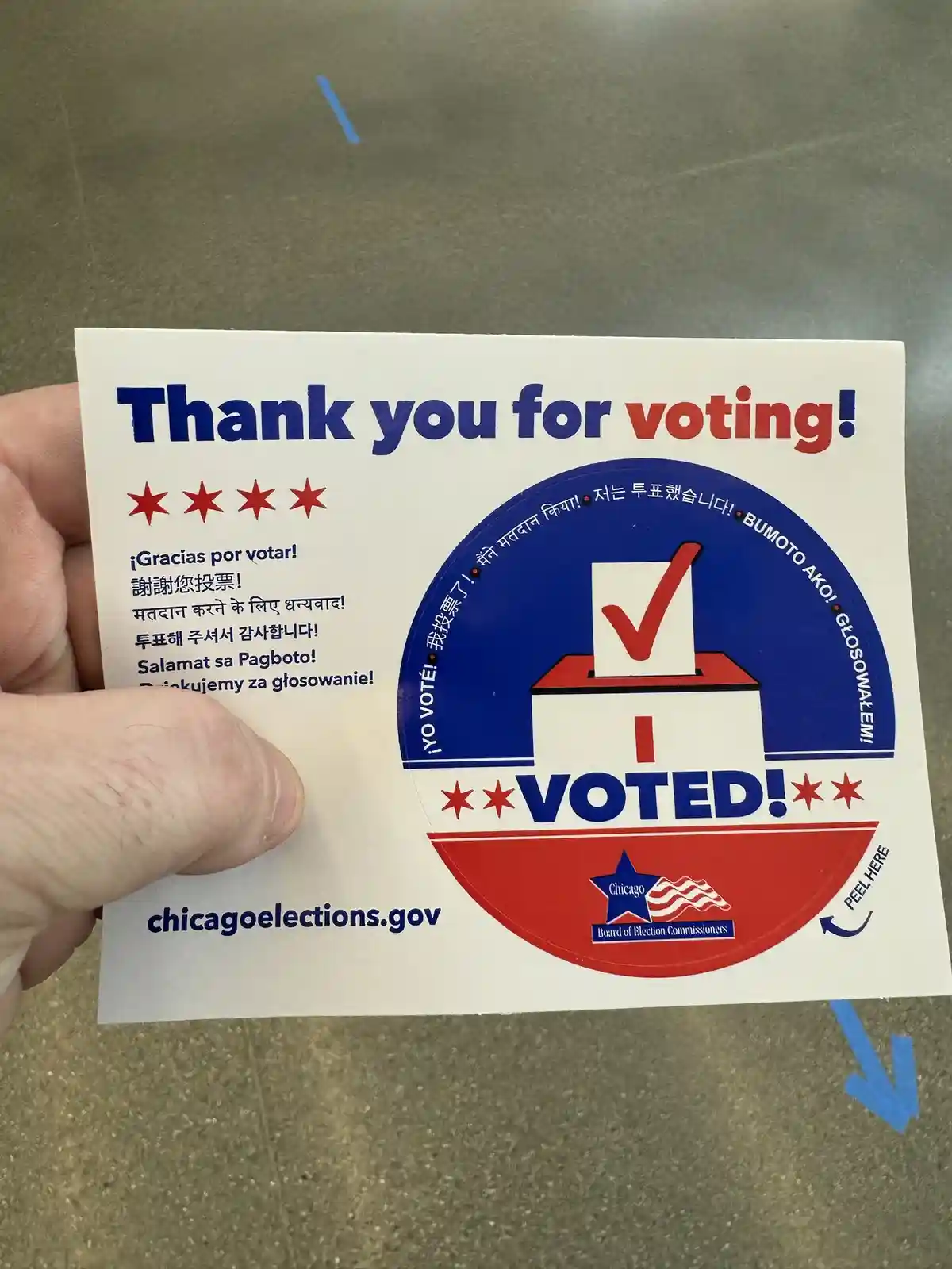 A hand holds a Chicago 'I Voted' sticker featuring a red, white, and blue design with a ballot box and checkmark. The…