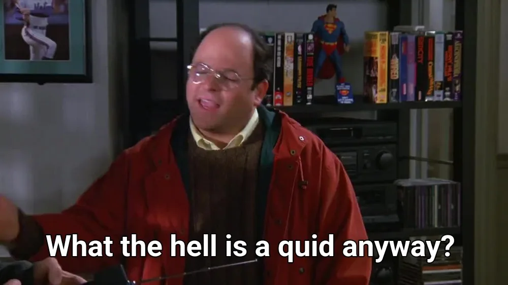 A man with glasses and a red jacket looks confused while holding a small object. Behind him, a shelf holds a Superman action…