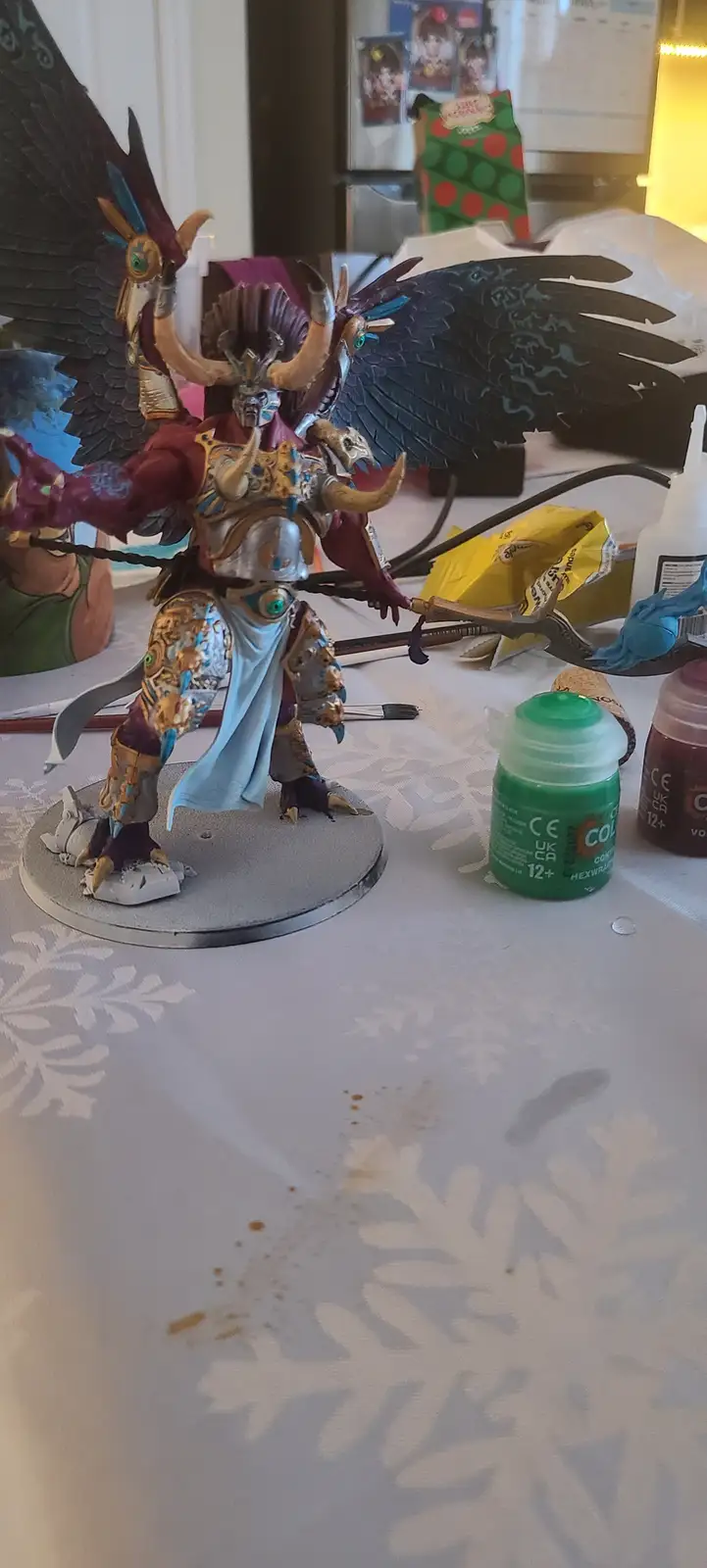 A highly detailed, painted fantasy miniature figure with large black wings, ornate armor, and a blue cape stands on a plain…