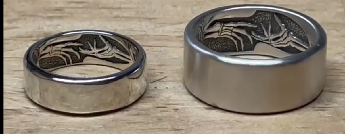 Two silver rings with spider skeleton engravings sit on a wooden surface, one smaller and one larger. The overlaid text…