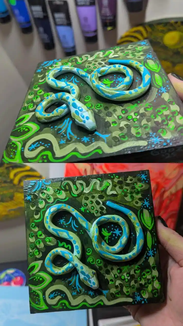 Two photos show a hand holding a square wooden art piece with a 3D painted snake coiled on it. The background is decorated…