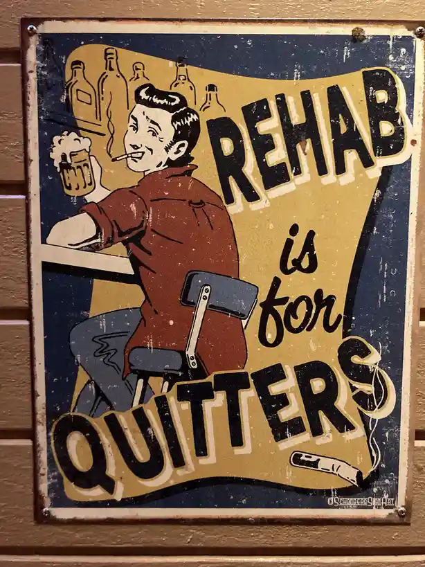 A vintage-style metal sign depicts a smiling man in a red shirt and blue pants sitting at a bar, holding a beer mug and…